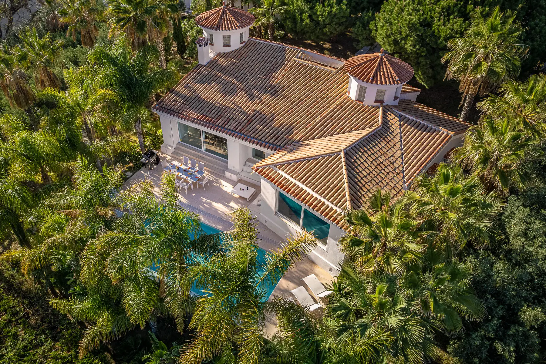 Oblique aerial view of a villa with a tiled roof and a pool, surrounded by palm trees