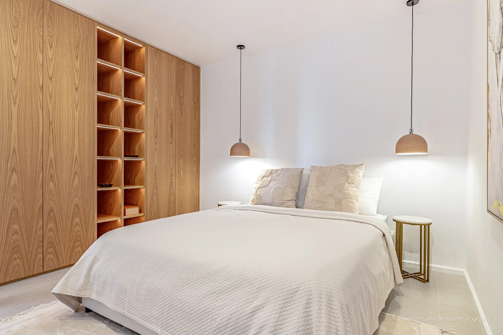 Dormitorio con carpintería de roble de suelo a techo, estantes iluminados y dos lámparas colgantes sobre la cama